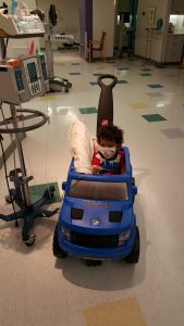Gavin riding a toy car on the hospital floor.