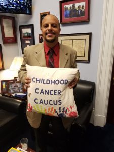 Sam Abdelmessih in Congressman Michael McCaul's DC Office holding the Childhood Cancer Caucus pillow